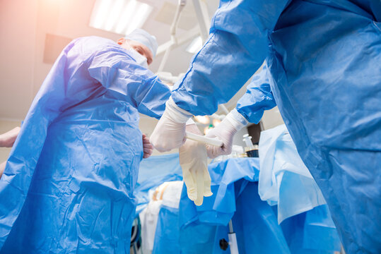 Assistant helps the surgeon put on latex gloves and surgical gown before the operation.