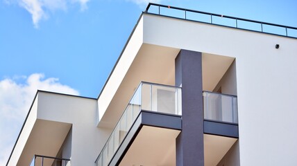 Fototapeta premium A fragment of modern architecture, walls and glass. Windows and balconies of a residential building against a blue sky. Detail of New luxury house and home complex. Part of city real estate property a