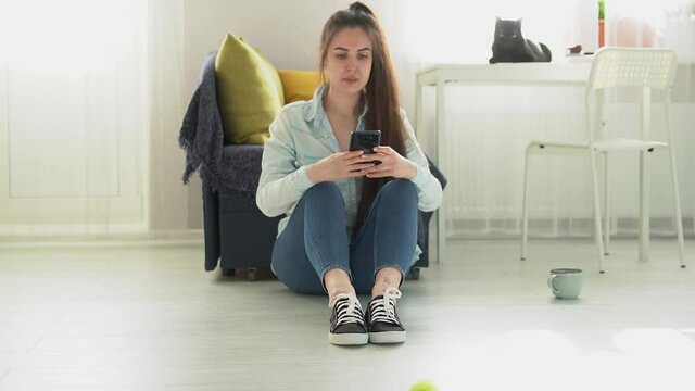 young woman sits on the floor at home and writes a message on the phone Slow motion HD