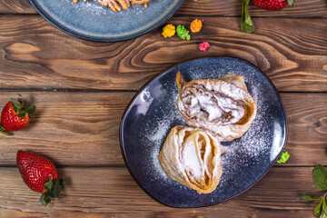 Sweet pastries, cakes, and pudding stand on a wooden table decorated with strawberries, limes, and other sweets.