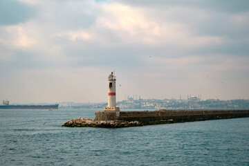 Lighthouse in bosporus with silhouette of grand ottoman mosques Hagia sophia (ayasofya) and blue (sultanahmet) mosques background with huge transportation ship sailing on the water.