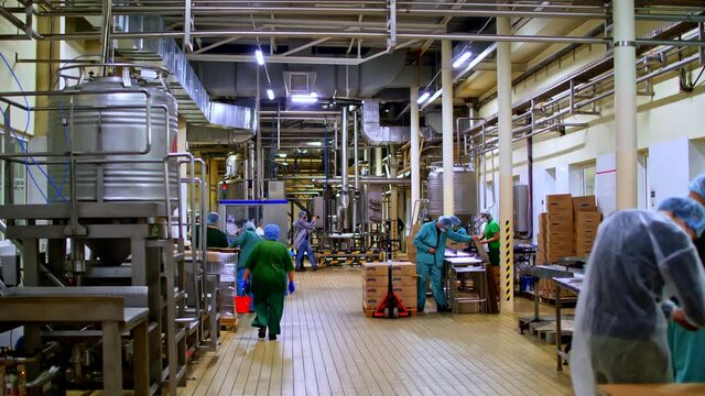 Employers of packing line, in bio resisting suits, filmed during the regular work process. View on a warehouse adapted to comply with quarantine restrictions