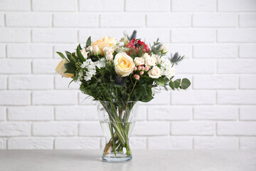 Beautiful bouquet with roses on grey table against white brick wall