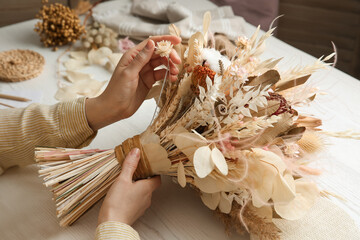 Florist making beautiful bouquet of dried flowers at white table, closeup