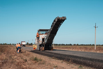 Machinery building of new road at the plain in sunny day. Work of asphalt paver with fields around