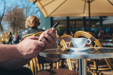 Man holds a smartphone on the background of a cup of coffee in a restaurant.