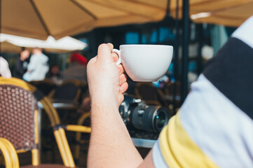 Photographer man drinks coffee in a restaurant on the background of a table with a camera.