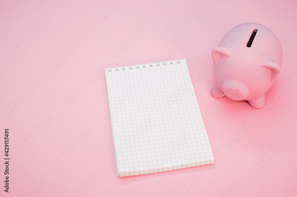 Poster top view of a notebook with a piggy bank isolated on a pink background