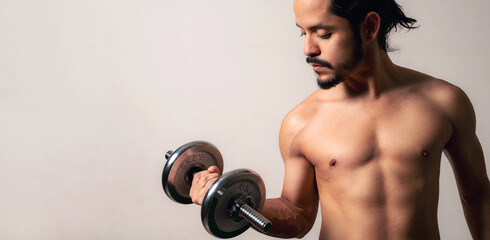 Young latin fitness man holding a metal dumbbell on a clear background with copy space