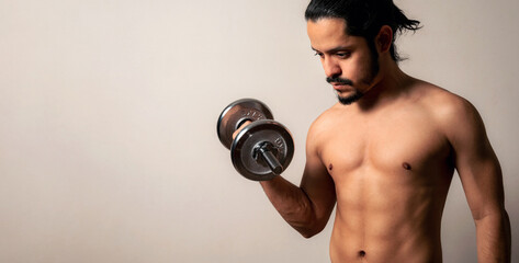 Fototapeta na wymiar Young latin fitness man holding a metal dumbbell on a clear background with copy space