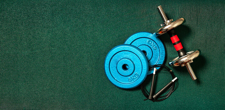 High angle view of exercise weights on a dark green blanket with copy space. Low light. Fitness equipment for exercising at home