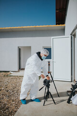 Man in a disposable coverall protective suit checking the camera on tripod while standing outdoor