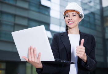 Woman architector in suit and hat is satisfied with realisation her project on the outside.