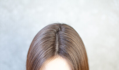 The head of a woman with a parting of gray hair. A woman does her hair. Brown hair on a woman's...