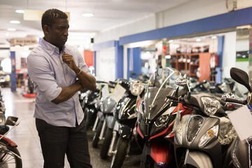 Fototapeta na wymiar Afro american man is shopping and choosing new motobike in moto store. High quality photo