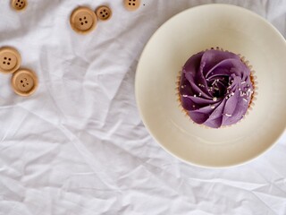 Pretty cupcake with purple frosting near wooden beads on a white textured background