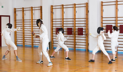 Adults and teens wearing the fencing uniform practicing with foil at the gym