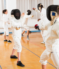 Portrait of kids and adults fencers with instructor engaged in fencing in training room