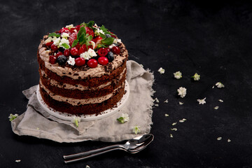 Delicious homemade chocolate cake with fresh berries and mascarpone cream on dark background.