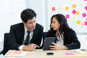 Multiethnic employee Caucasian woman and the Asian man use tablet to discuss about a work schedule at the office. Happy teamwork colleagues have brainstorming in the workplace on a business day.