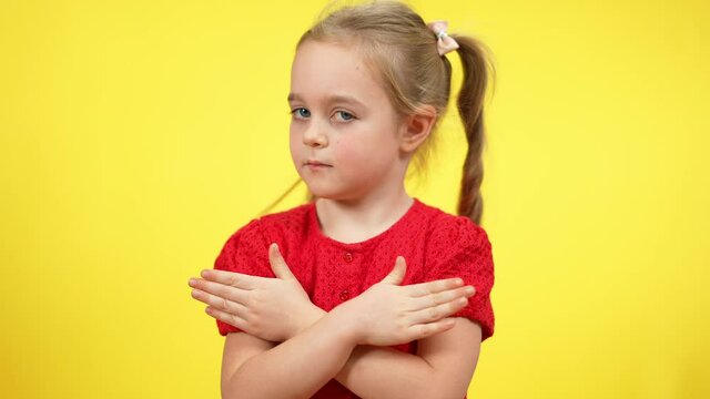 Portrait of serious cute little girl with pigtails and crossed hands looking at camera shaking head no. Unhappy Caucasian child posing at yellow background. Rejection and refusal concept