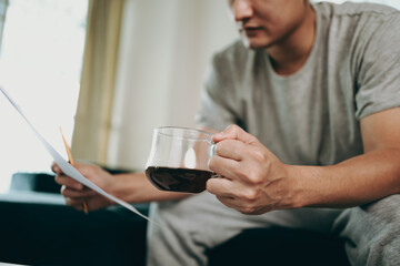 Young Businessman working at home with paper graph and data sheet and he is dirnk coffee. Business and freelance concept.