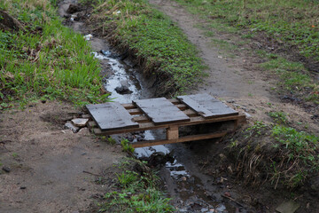 Fototapeta premium A small homemade wooden bridge over a muddy, smelly puddle or stream in a slum. Unkempt area, outskirts of the city.