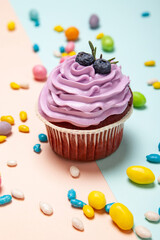 Delicious cupcake near sweet candies on peach and blue background