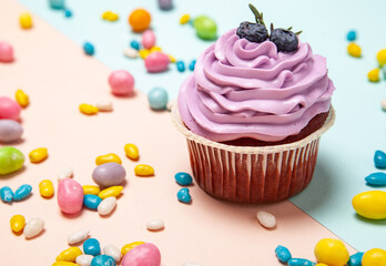 Delicious cupcake near sweet candies on peach and blue background
