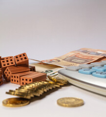 Pile of bricks, coins and euro notes next to a calculator on a white background. Home loan real estate for mortgage concept