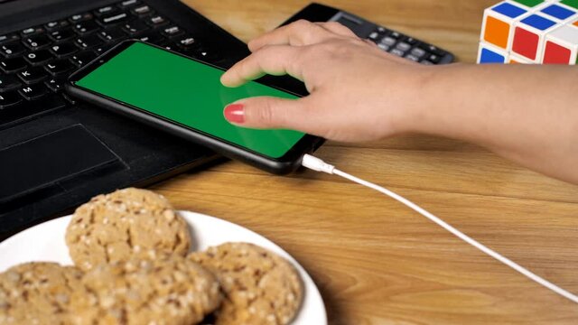 Lady's hand connecting earphone cable to listen to soothing music during work. Green screen chroma key device on the laptop with eatables  calculator  Rubik's cube on a businesswoman's desk