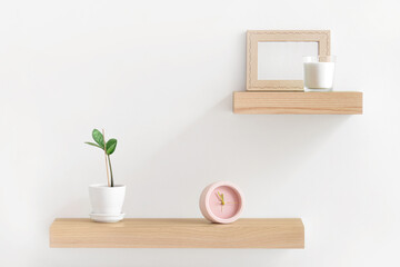 Wooden shelves with alarm clock, houseplant and photo frame on white wall