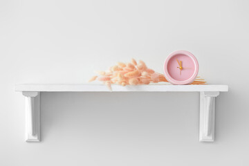 Shelf with alarm clock and spikelets on white wall