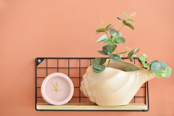 Modern shelf with alarm clock and houseplant on color wall