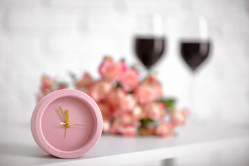 Alarm clock with flowers and glasses of wine on table in room