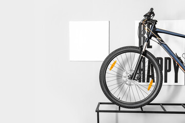Modern bicycle on stand near white wall with pictures