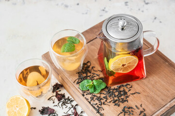 Teapot and glasses of tasty black tea with lemon and mint on light background