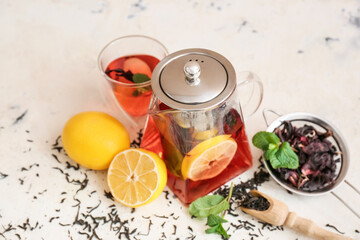 Teapot and glass of tasty black tea with lemon and mint on light background
