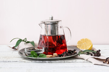 Teapot of tasty hibiscus tea with lemon and mint on light wooden background