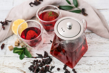 Teapot and glasses of tasty hibiscus tea with lemon on light wooden background