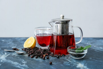 Teapot and glass of tasty hibiscus tea with lemon on color background