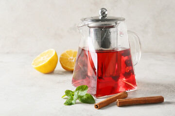 Teapot of tasty tea with lemon, mint and cinnamon on light background