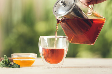 Woman pouring tasty tea from teapot into glass on table outdoors