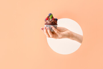 Female hand with tasty chocolate cupcake on color background