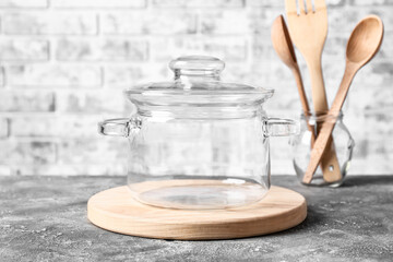 Stylish cooking pot and utensils on table against brick wall