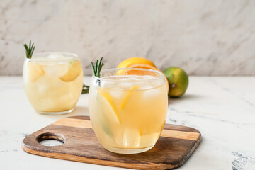 Glass of cold tea with rosemary and citrus fruits on light background