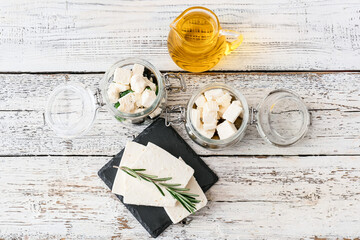 Jars with tasty feta cheese, oil and olives on light wooden background