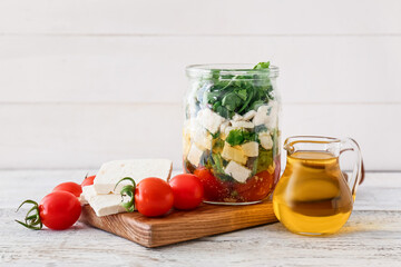 Jar with tasty feta cheese, oil and tomatoes on light wooden background