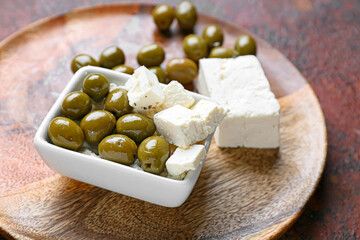 Bowl with tasty feta cheese and olives on grunge background, closeup