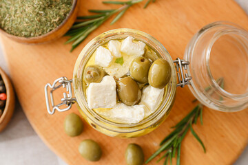 Jar with tasty feta cheese, oil and olives on wooden background
